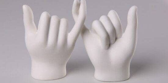 A white sculpture of two hands with intertwined pinky fingers.